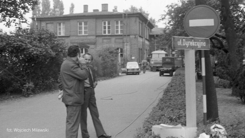 Zdjęcie archiwalne, dwaj mężczyźni stoją w świetle ulicy, w tle budynek i słupek z nazwą ulicy: Dyrekcyjna