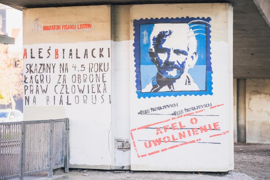 Mural na filarze wiaduktu przedstawia widok niebieskiego znaczka pocztowego z twarzą Alesia Bialackiego i napisy dotyczące walki o prawa człowieka i demokrację na Białorusi