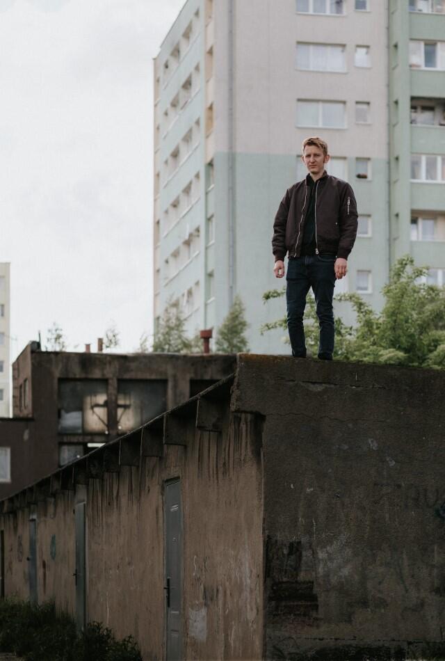 młody mężczyzna stoi na murku, w tle biały wieżowiec