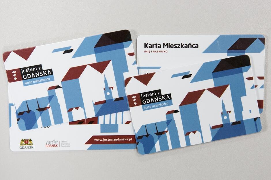 Zdjęcie przedstawia kilka leżących obok siebie gdańskich Kart Mieszkańca. Są wielkości karty bankomatowej, w tonacji kolorystycznej biało-niebieskiej. W lewym górnym karty jest logo z tarczą herbową Gdańska i napis "Jestem z Gdańska" 