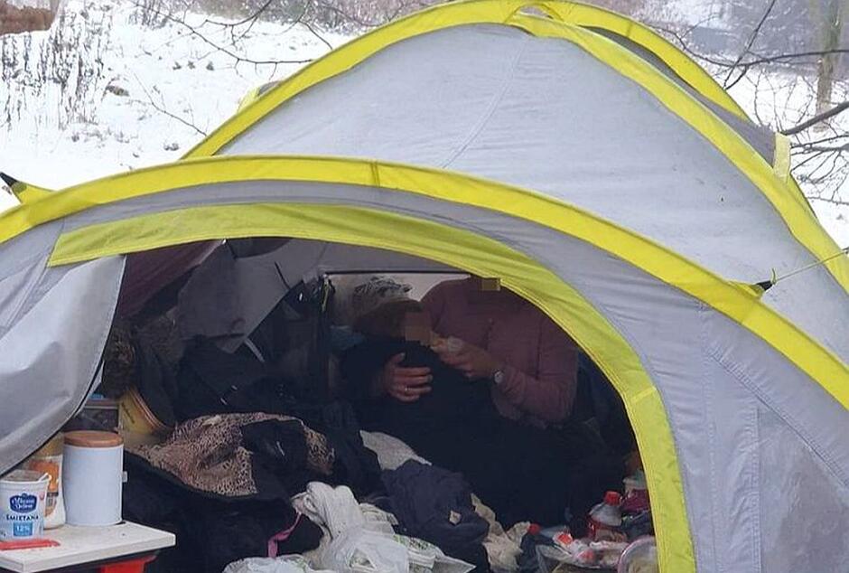namiot, we wnętrzu siedzi kobieta z dzieckiem dookoła mnóstwo przedmiotów i śnieg