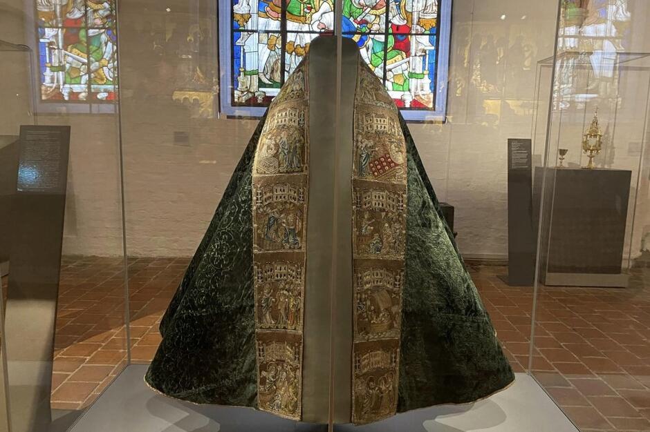 Szata liturgiczna - rodzaj obszernego płaszcza zarzucanego na plecy kapłana. Kolory zielony i złoty. Szata eksponowana jest w szklanej gablocie, znajduje się na statywie 