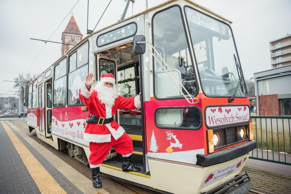 Zabytkowy tramwaj przystrojony świątecznymi ozdobami. W pierwszych drzwiach stoi Św. Mikołaj w tradycyjnym czerwonym stroju.