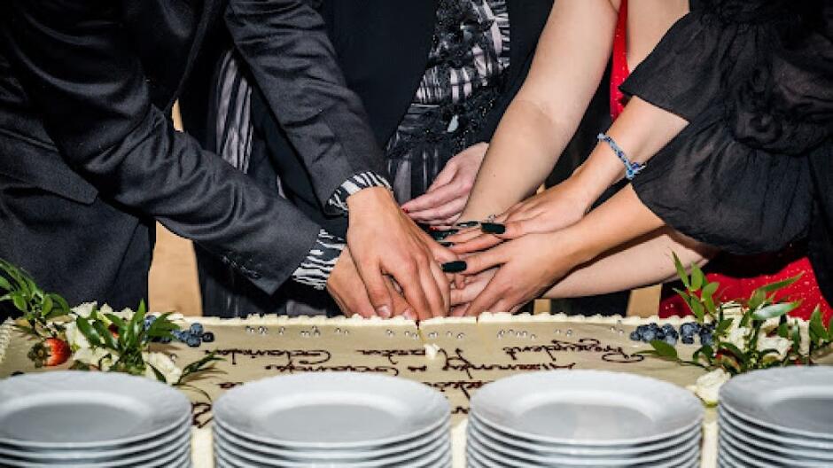 Białe talerzyki ustawione w stos i ręce kilku osób krojących wspólnie tort