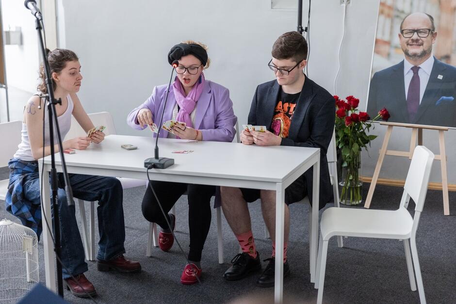 dwie nastolatki i nastolatek siedzą przy stole i grają w karty