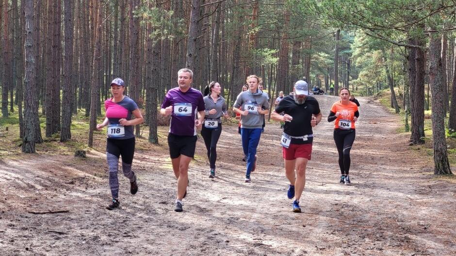 Kilka osób, kobiet i mężczyzn, biegnących w lesie