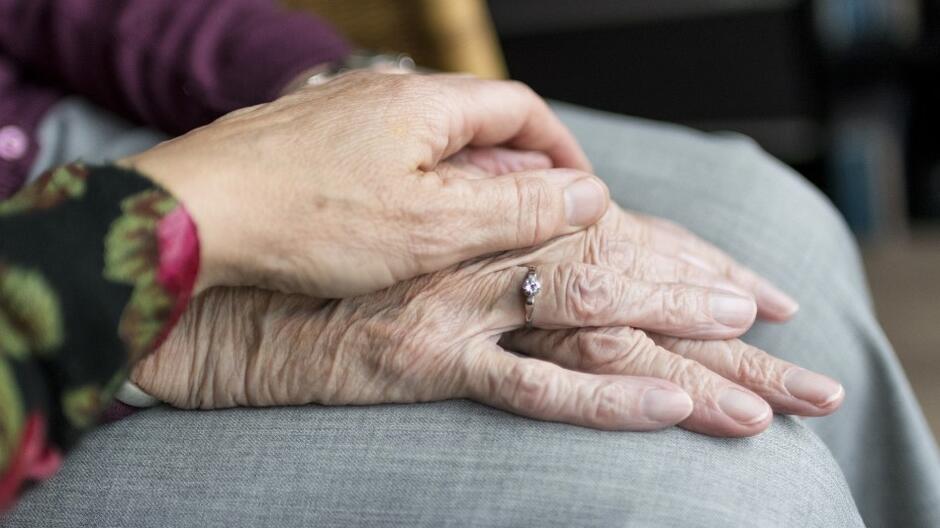 Młoda dłoń kobiety dotyka starszą dłoń kobiety z pierścionkiem na palcu