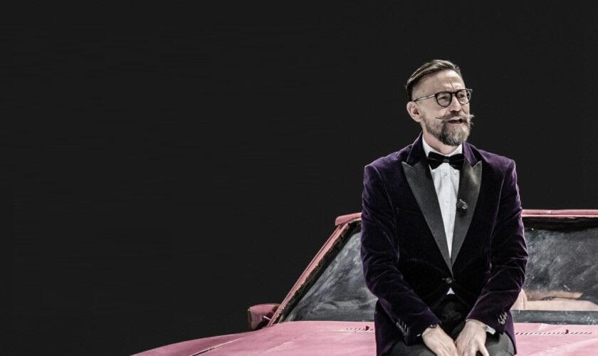 mężczyzna w okularach i w garniturze oparty o różowe auto
