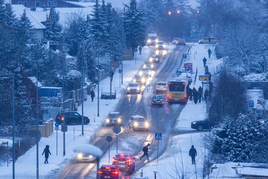 ogólny widok zaśnieżonej, wieczornej ulicy, widać dużo samochodów i pieszych