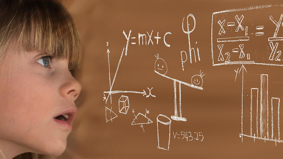 kilkuletnia dziewczynka na tle tablicy pełen wzorów matematycznych napisanych kredą