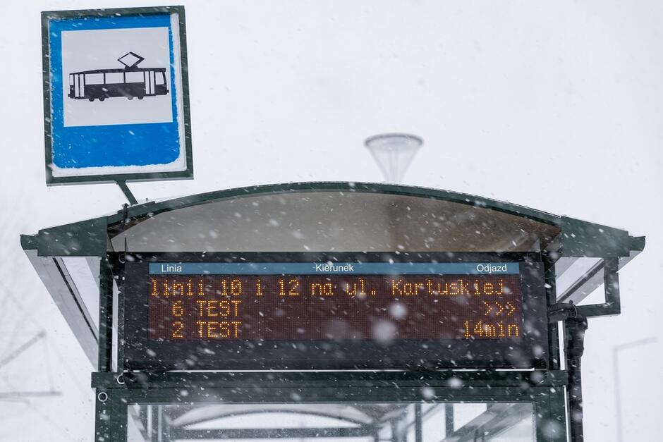 na zdjęciu tablica informacyjna wisząca przy wiacie przystankowej, informuje o testowych jazdach tramwaju na trasie