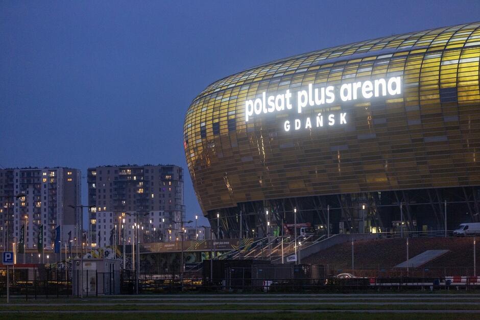 Widok stadionu wieczorową porą, z podświetlonym napisem: Polsat Plus Arena Gdańsk