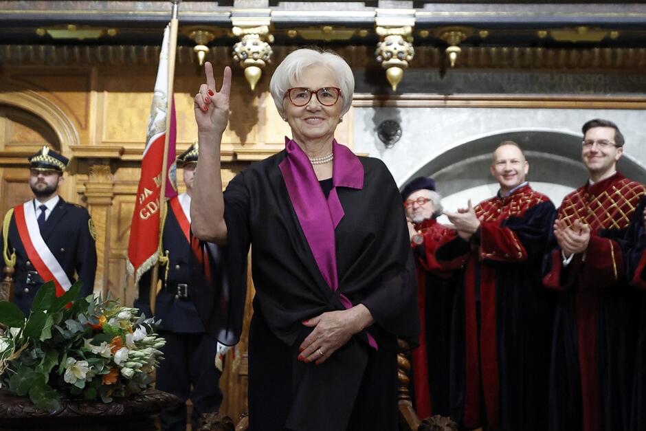 starsza kobieta pozuje uśmiechnięta z palcami ułożonymi w literę V