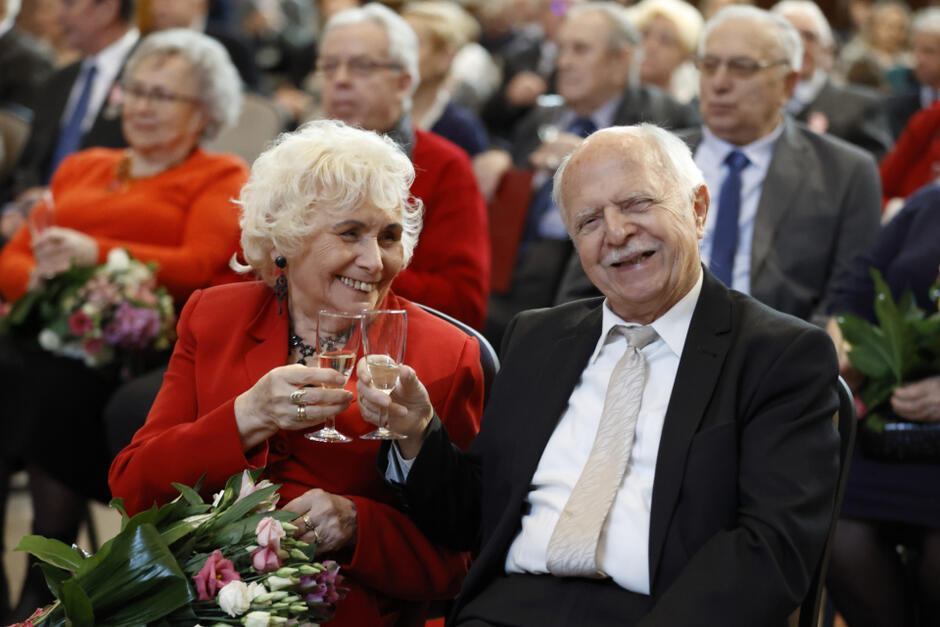 uśmiechnięta para odświętnie ubranych seniorów pozuje z lampkami szampana