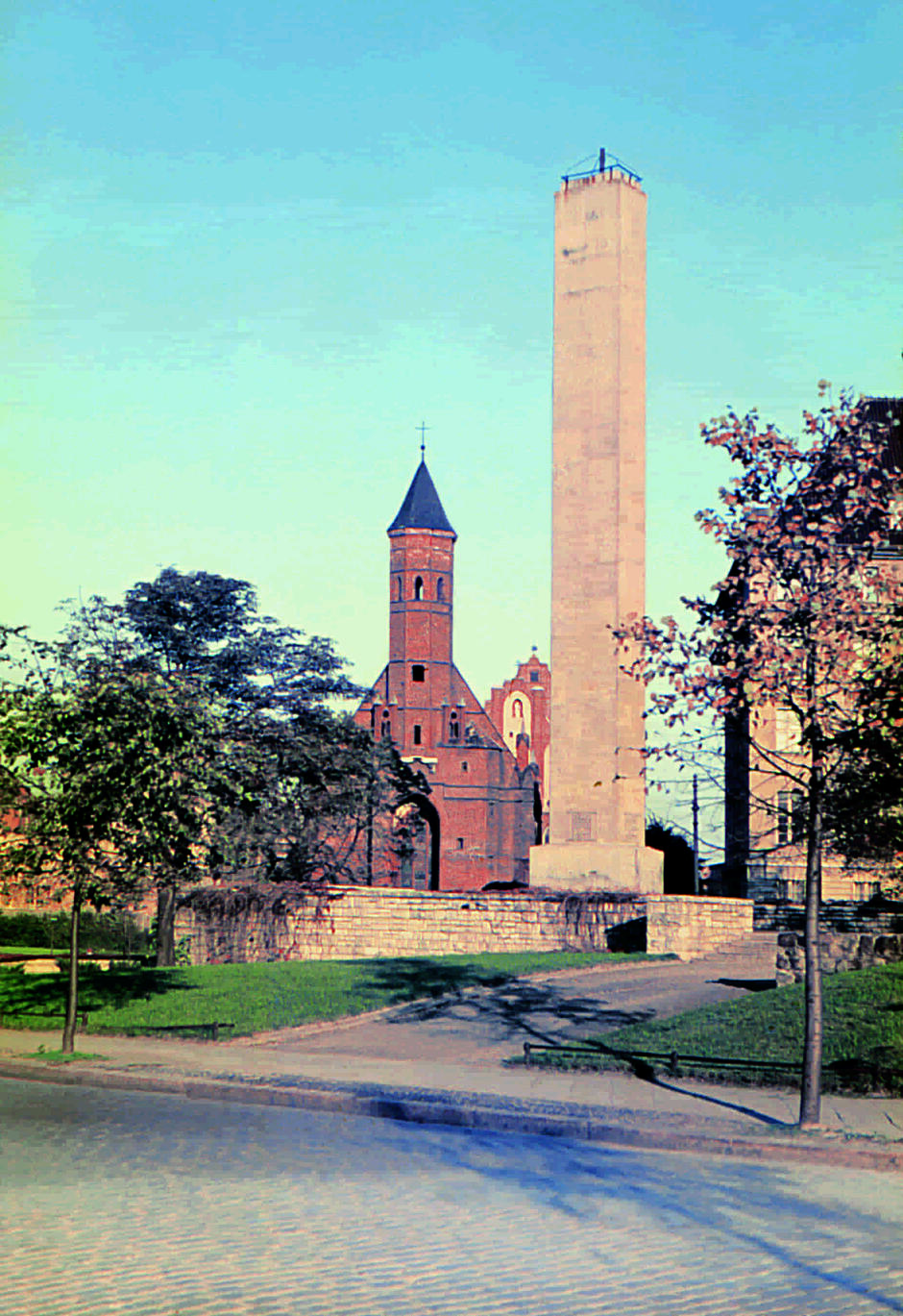 Pionowy, wysoki obelisk na tle kościoła gotyckiego 
