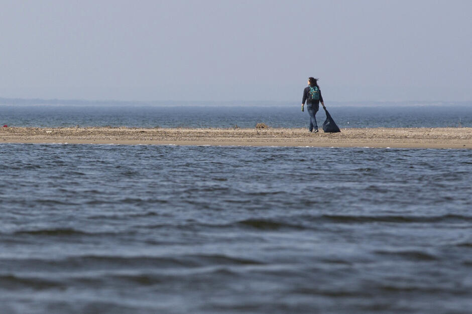 Zdjęcie przedstawia człowieka stojącego na plaży, nad brzegiem morza 