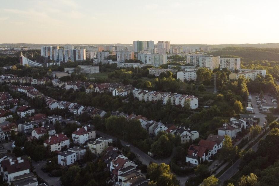 zdjęcie z drona, na pierwszym planie widać domki jednorodzinne szeregowo ustawione, w tle wysoka i szeroka zabudowa mieszkaniowa, widać różnej wielkości i szerokości budynki