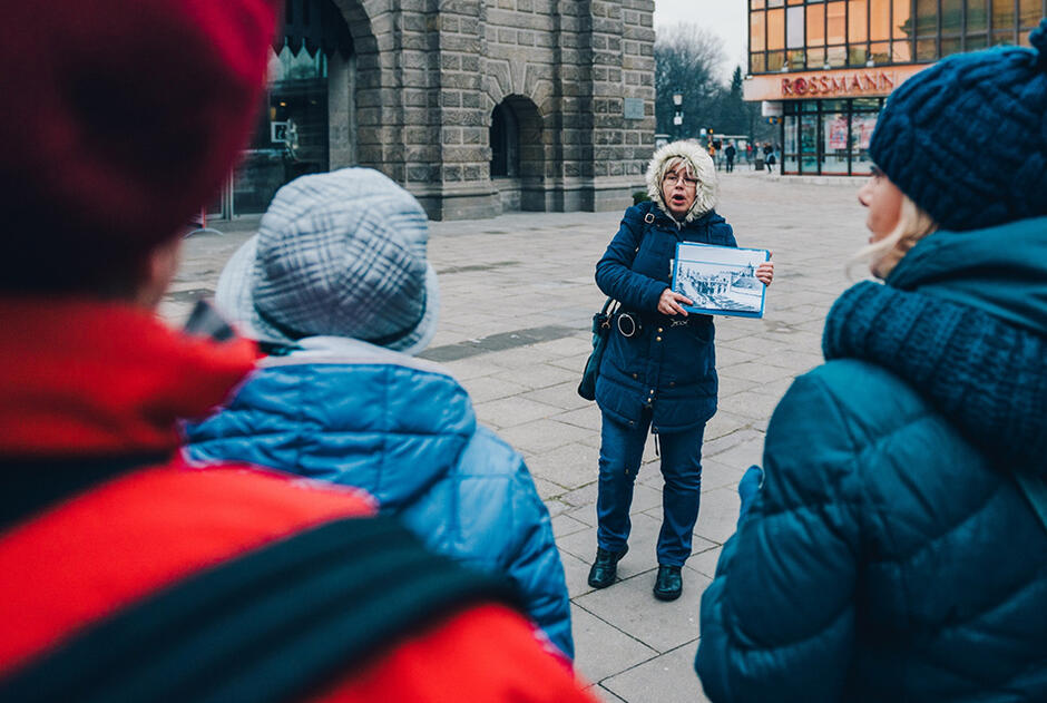 Przewodnik trzymający w ręku planszę ze zdjęciem mówiący do turystów
