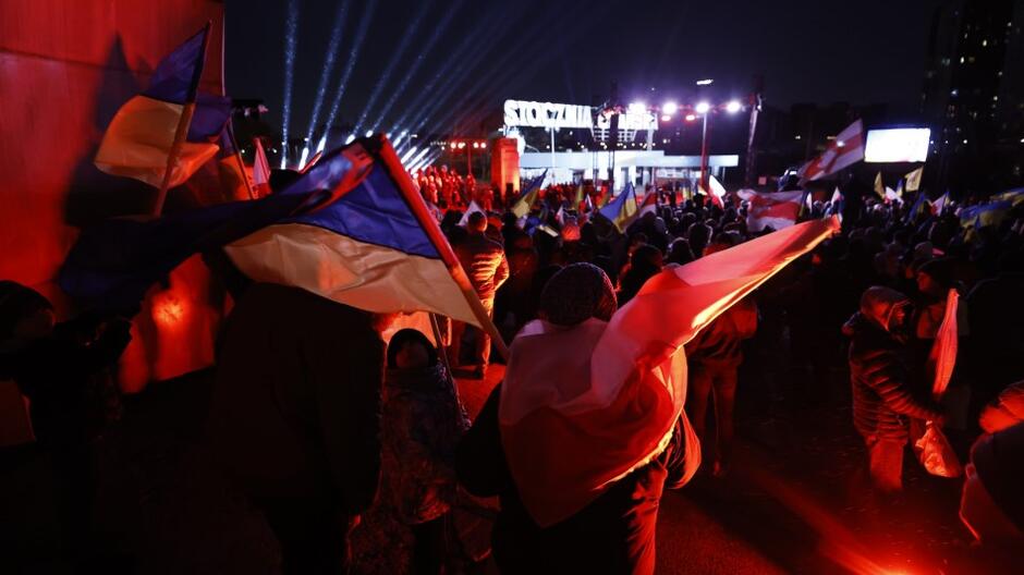 Grupa osób podczas wieczornej manifestacji, w tle napis Stocznia Gdańska