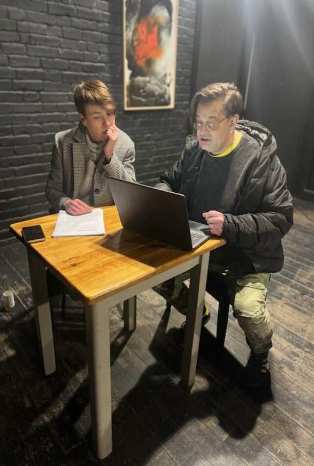 kobieta i mężczyzna siedzą przy stoliku, przez nią leży kartka papieru, przed nim stoi laptop