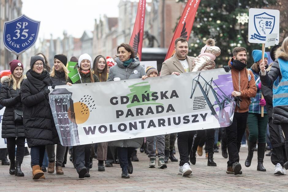 Grupa osób, idących ulicą z transparentem Gdańska Parada Wolontariuszy 