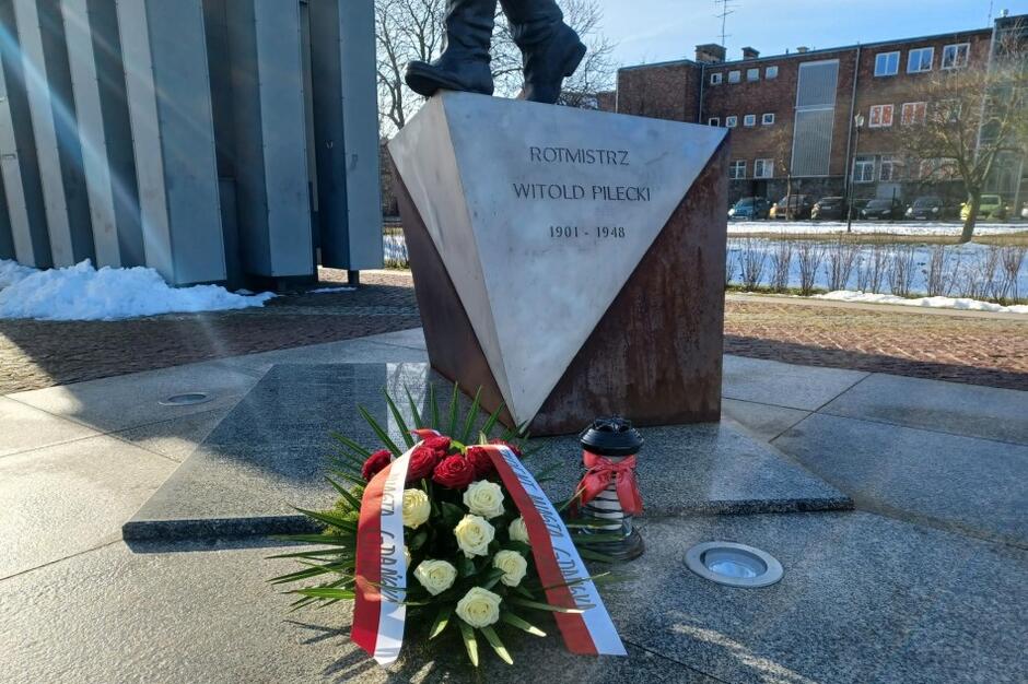 Przed cokołem pomnika leży wieniec z biało-czerwonymi wstążkami, ustawiony jest też nagrobkowy znicz