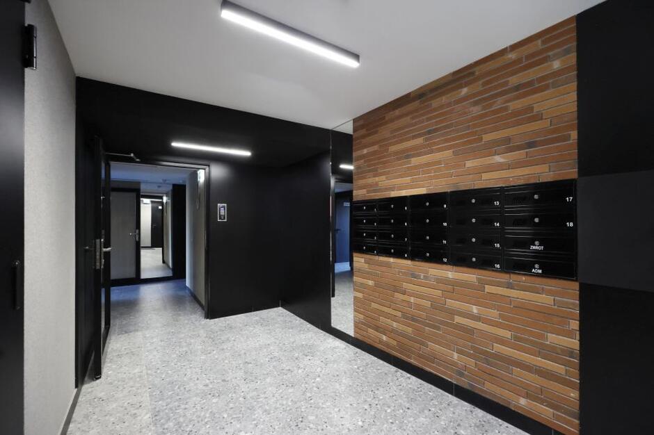 korytarz nowoczesny, ciemno-drewniane materiały wykończeniowe, szklane drzwi i ciemne skrzynki na listy
