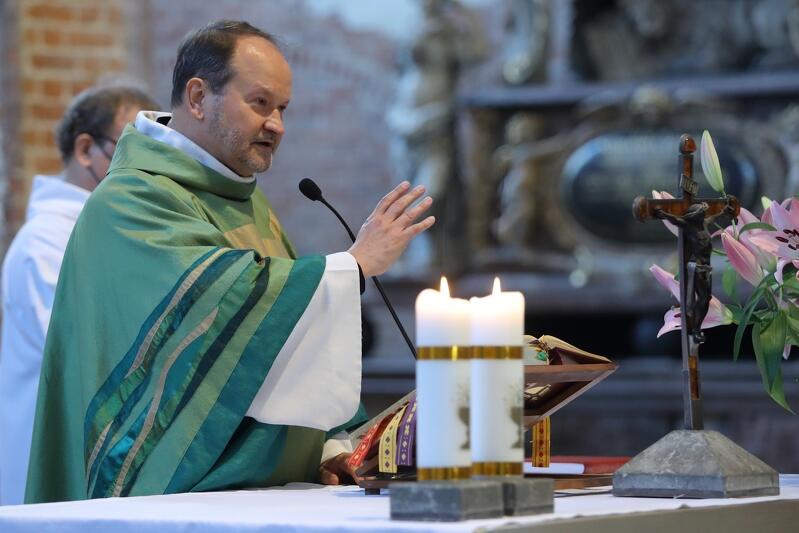 kapłan w stroju liturgicznym stoi za ołtarzem i wykonuje gest błogosławieństwa