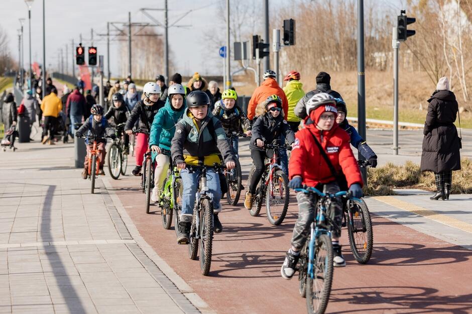 mali i młodzi rowerzyści, ubrani zimowo jadą tłumnie drogą rowerową