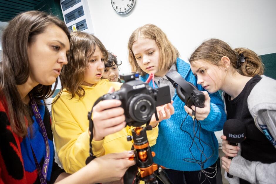 Kilkoro dzieci przy aparacie fotograficznym - na twarzach widać duże zainteresowanie aparatem