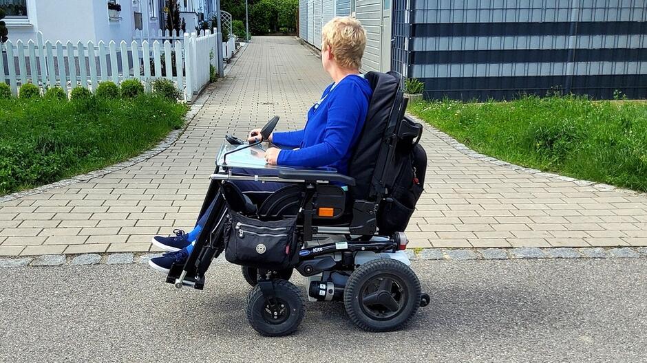 Kobieta na wózku inwalidzkim, w tle ulica i budynki mieszkalne
