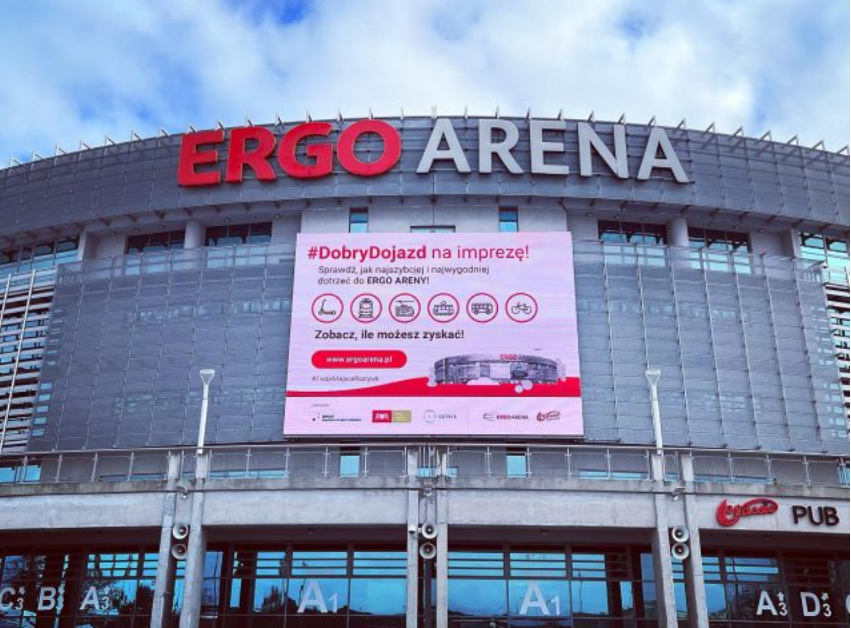na zdjęciu fragment hali ergo arena, na jej elewacji wywieszony jest jasny baner