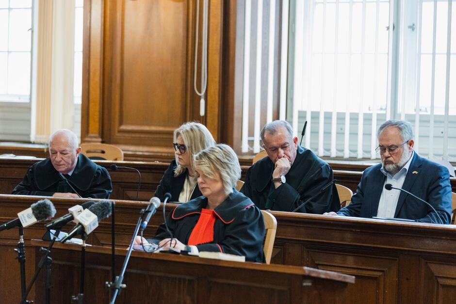 Kilka osób ubranych m.in. w togi siedzących na sali sądowej