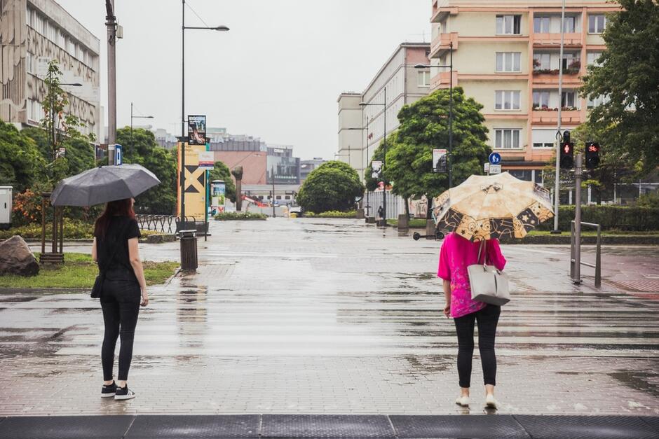 dwie kobiety z parasolkami stoją przy przejściu dla pieszych