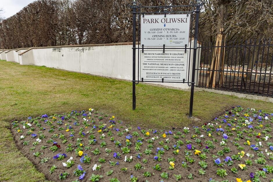 na zdjęciu biała tablica z napisem park oliwski, pod nią rabata na której zasadzono kilkadziesiąt kwiatków, w tle zielony trawnik