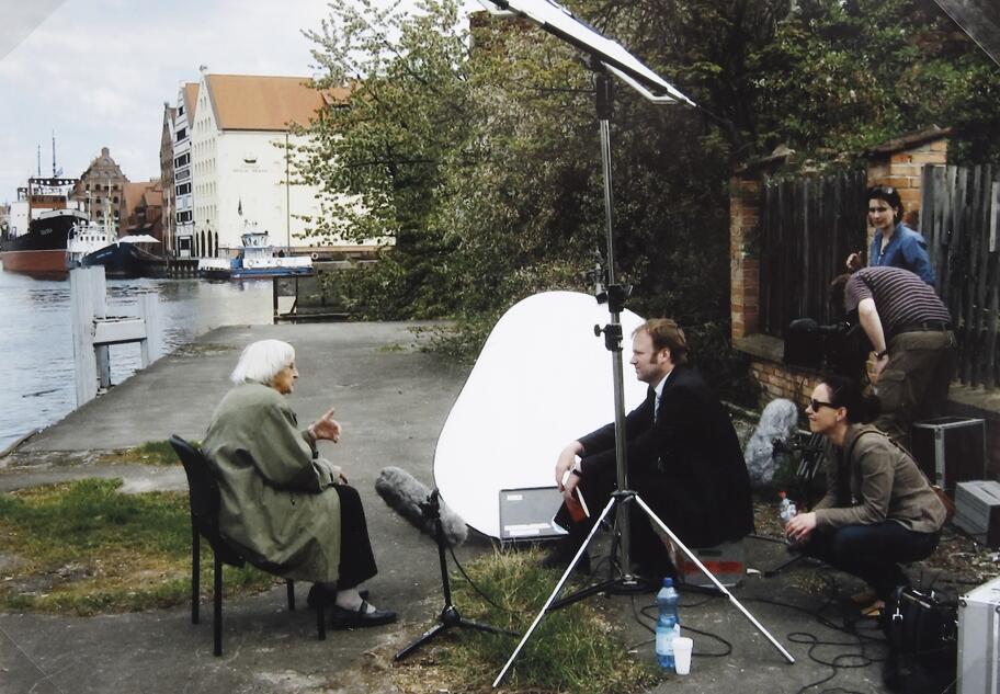 starsza pani siedzi na krześle w plenerze Gdańska, filmuje ją ekipa