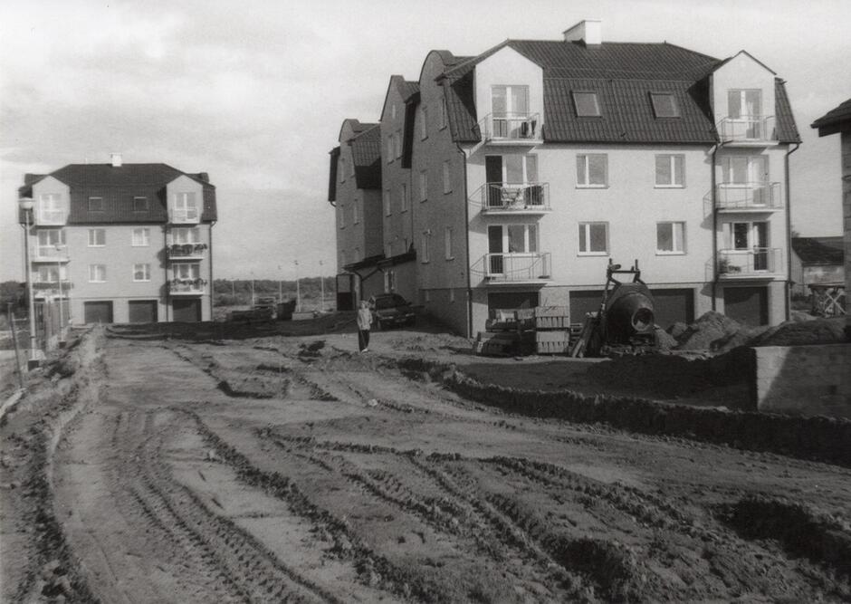 Czarno-białe zdjęcia: na pierwszym planie droga piaszczysta, w tle dwa budynki mieszkalne