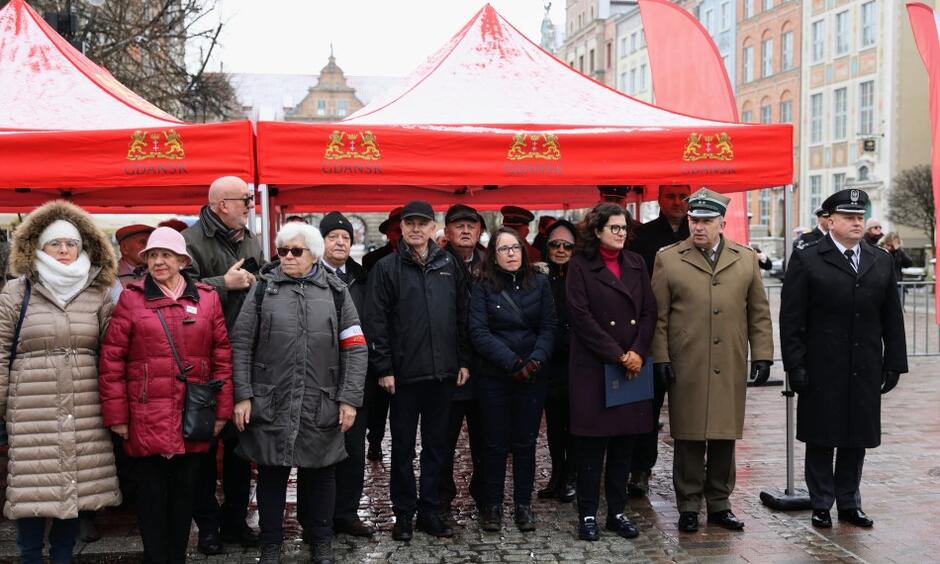 Grupa kilkunastu osób stojąca pod namiotem w zimowy dzień w centrum zabytkowego Gdańska