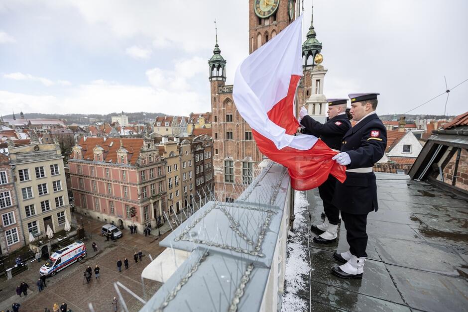Marynarze wieszający biało-czerwoną flagę na dachu budynku