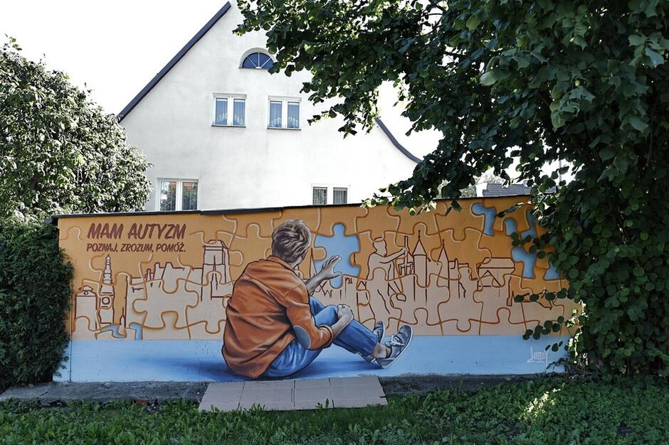 Mural dotyczący autyzmu: siedząca osoba, po lewej napis: MAM AUTYZM. POZNAJ, ZROZUM, POMÓRZ 