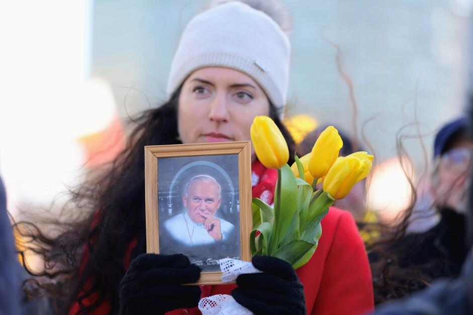 Kobieta trzymająca w ręku zdjęcie Jana Pawła II oraz żółte tulipany 