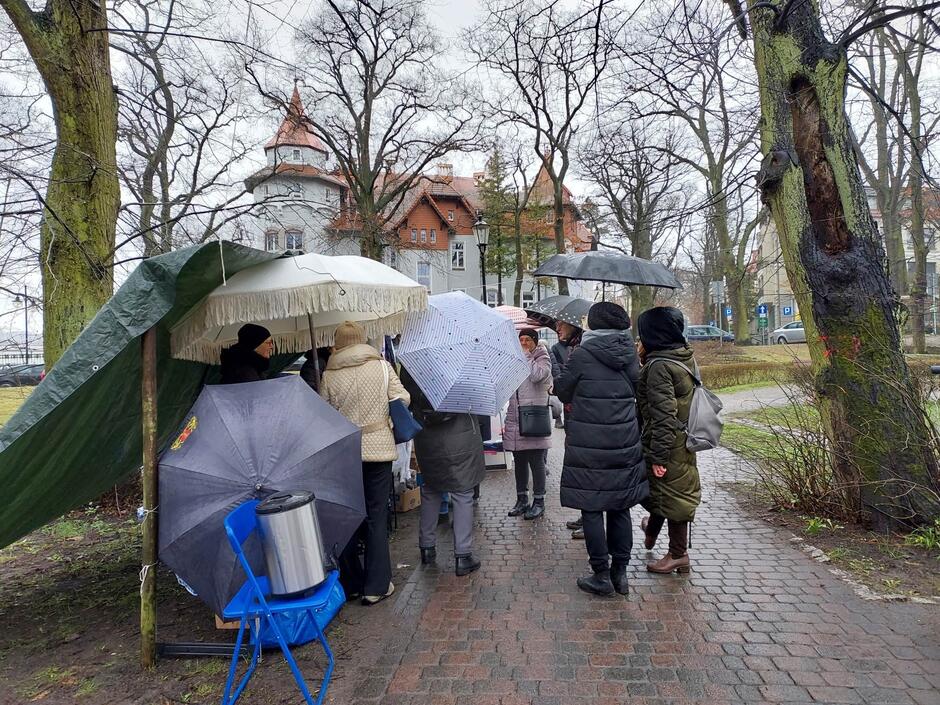 na zdjęciu kilka osób z parasolami, stoją w grupie w jednym miejscu
