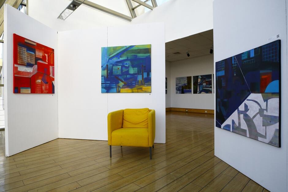 Wystawa w Żaku, na ścianach wiszą duże kolorowe graficzne obrazy, na środku stoi żółty fotel