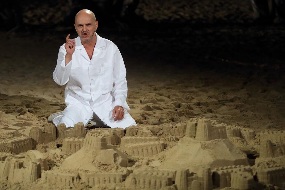 ubrany na biało mężczyzna siedzi na scenie wysypanej piaskiem