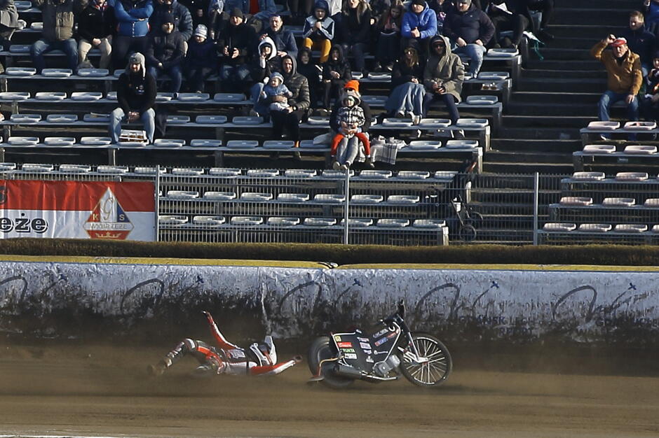 Zawodnik leży na torze, obok motor, w tle banda toru