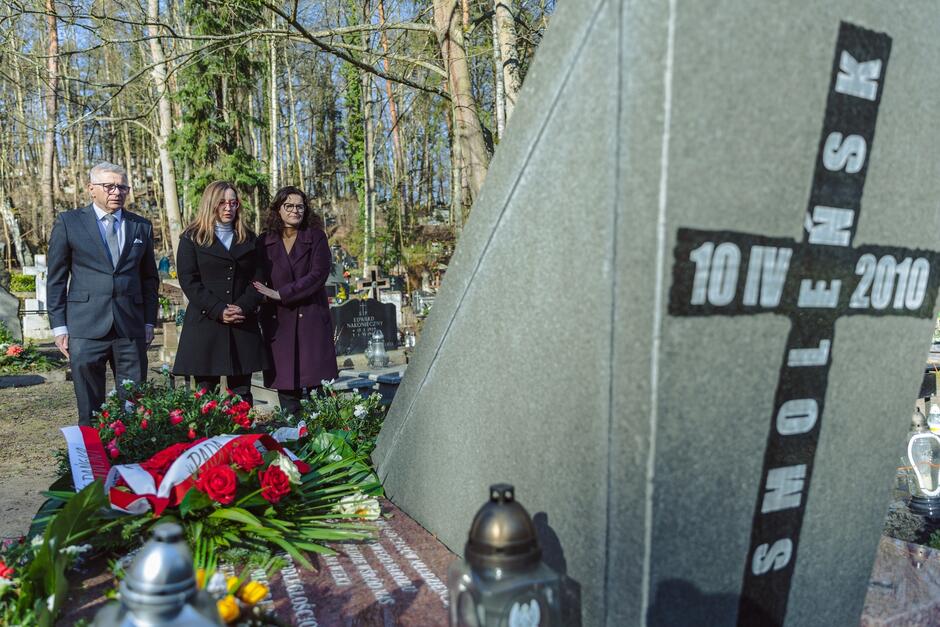 Trzy osoby stoją przed grobem. Na jego tyle napis: SMOLEŃSK, 10 IV 2010