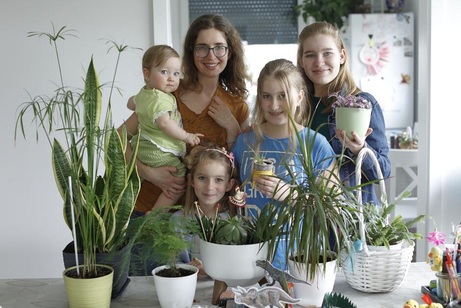 wymieniona kobieta i jej córki w wieku od 10 miesięcy do 14 lat pozują przed stołem z doniczkami z roślinnością