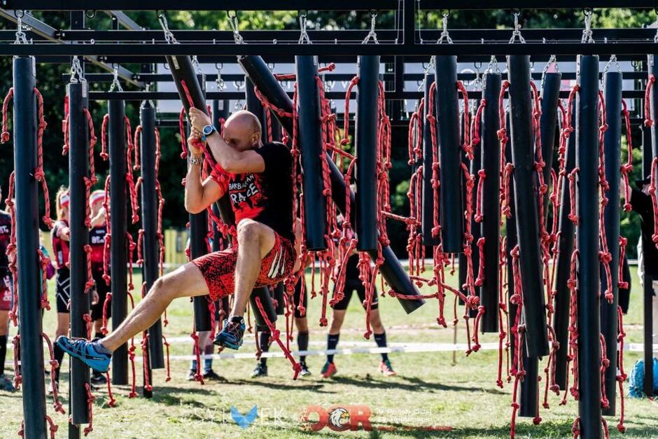 przeszkoda z lin, pokonuje ją zwisający na linie mężczyzna w stroju sportowym
