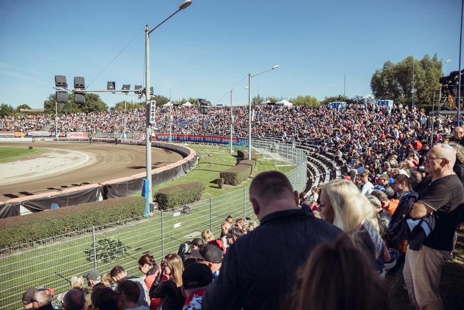 stadion żużlowy z bieżnią, na trybunach siedzą tłumy widzów