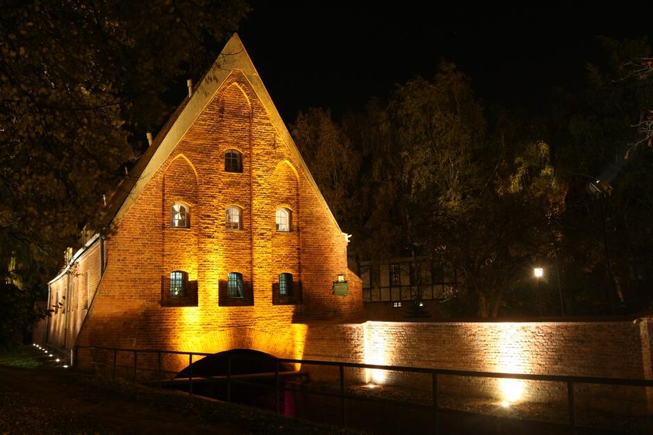 średniowieczny, ceglany budynek nad kanałem nocą, podświetlony iluminacją